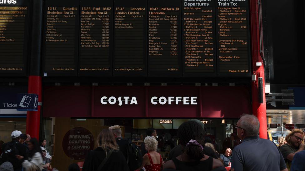 Passengers stand looking at departure boards at Liverpool Lime Street railway station as disruption continues