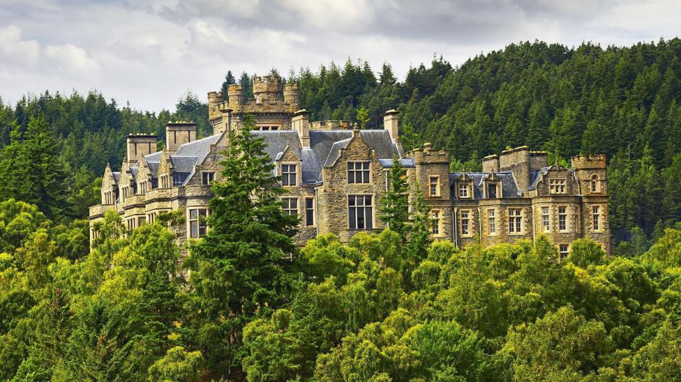 Carbisdale Castle is a large property in Scottish baronial style. The top floors of the house rise above a heavily wooded area.