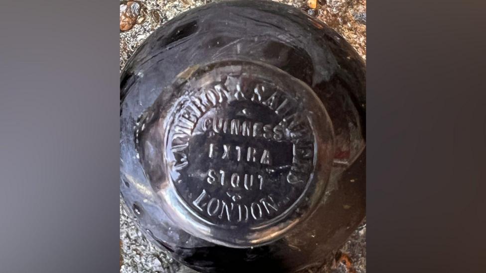 A black bottle. Written on the top of the cap is 'GUINNESS EXTRA STOUT LONDON'.