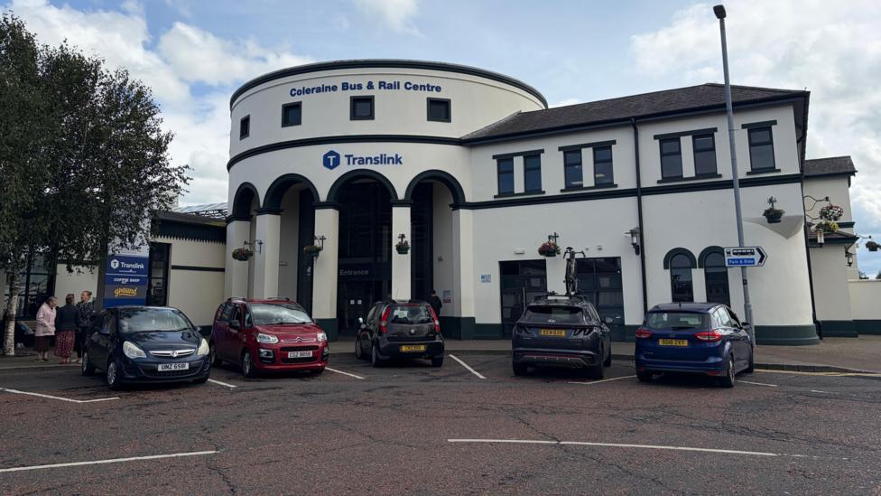 Coleraine train station, a large white building with cars parked outside. A sign on the top of the building reads