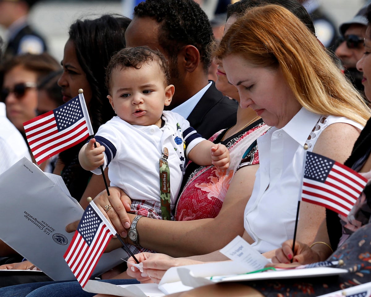 A baby in its mother's arms plays with a US flag.