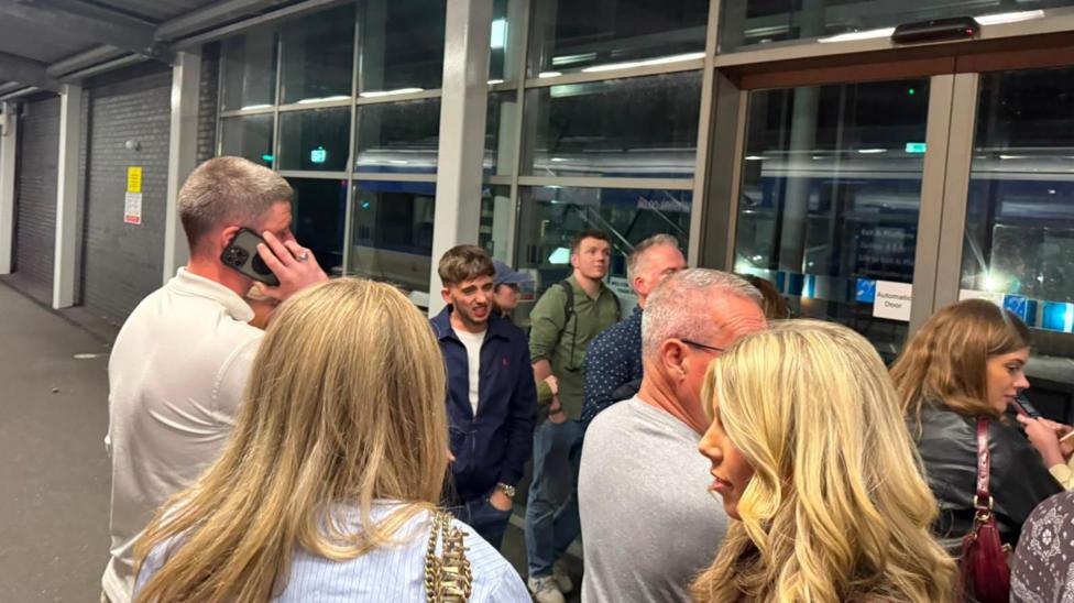 Another group of passengers wait at a train station doorway. One man is holding a mobile phone to his ear.