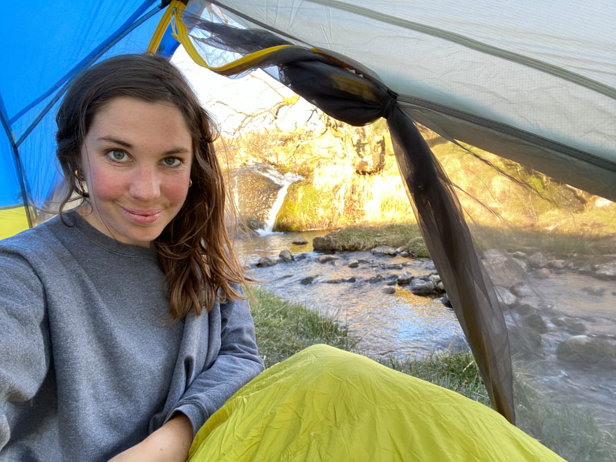 Young woman smiling in a tent with a river behind.