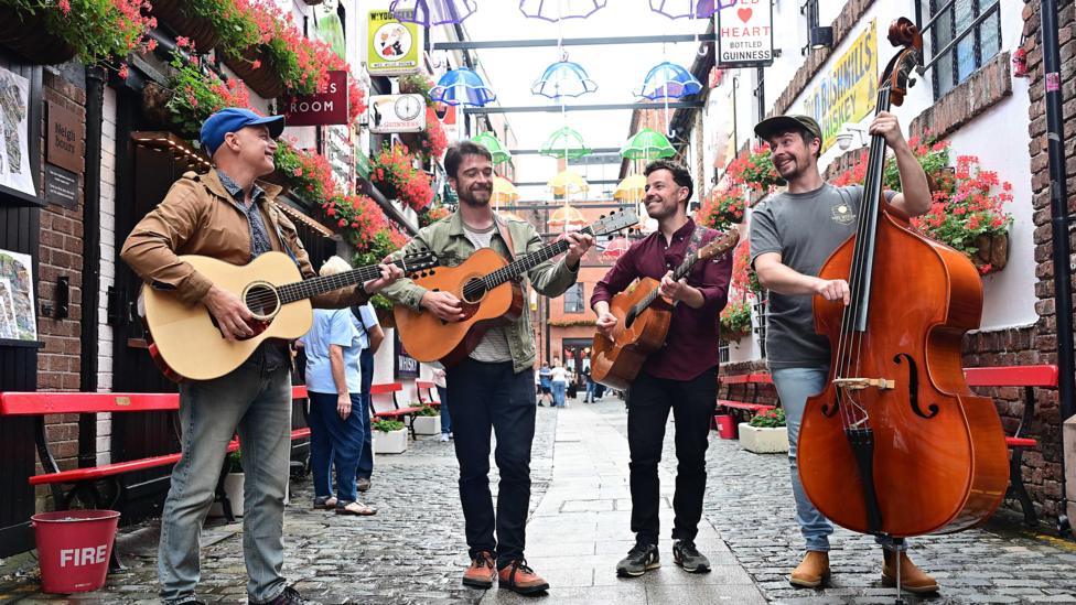 three men with guitars and one man with a cello in the Cathedral quarter in Belfast