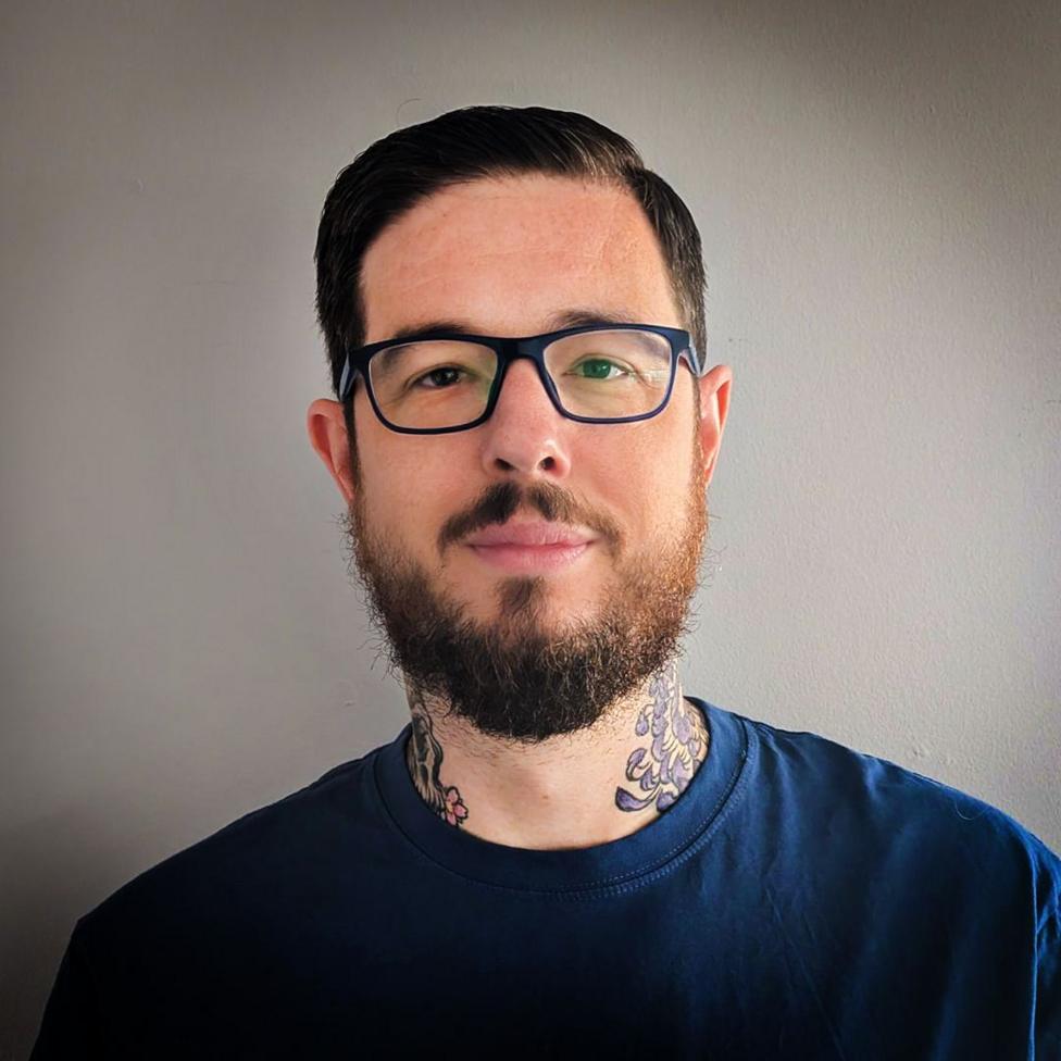 A headshot of Dr Michael Rees who is wearing a black t-shirt and standing against a white background.