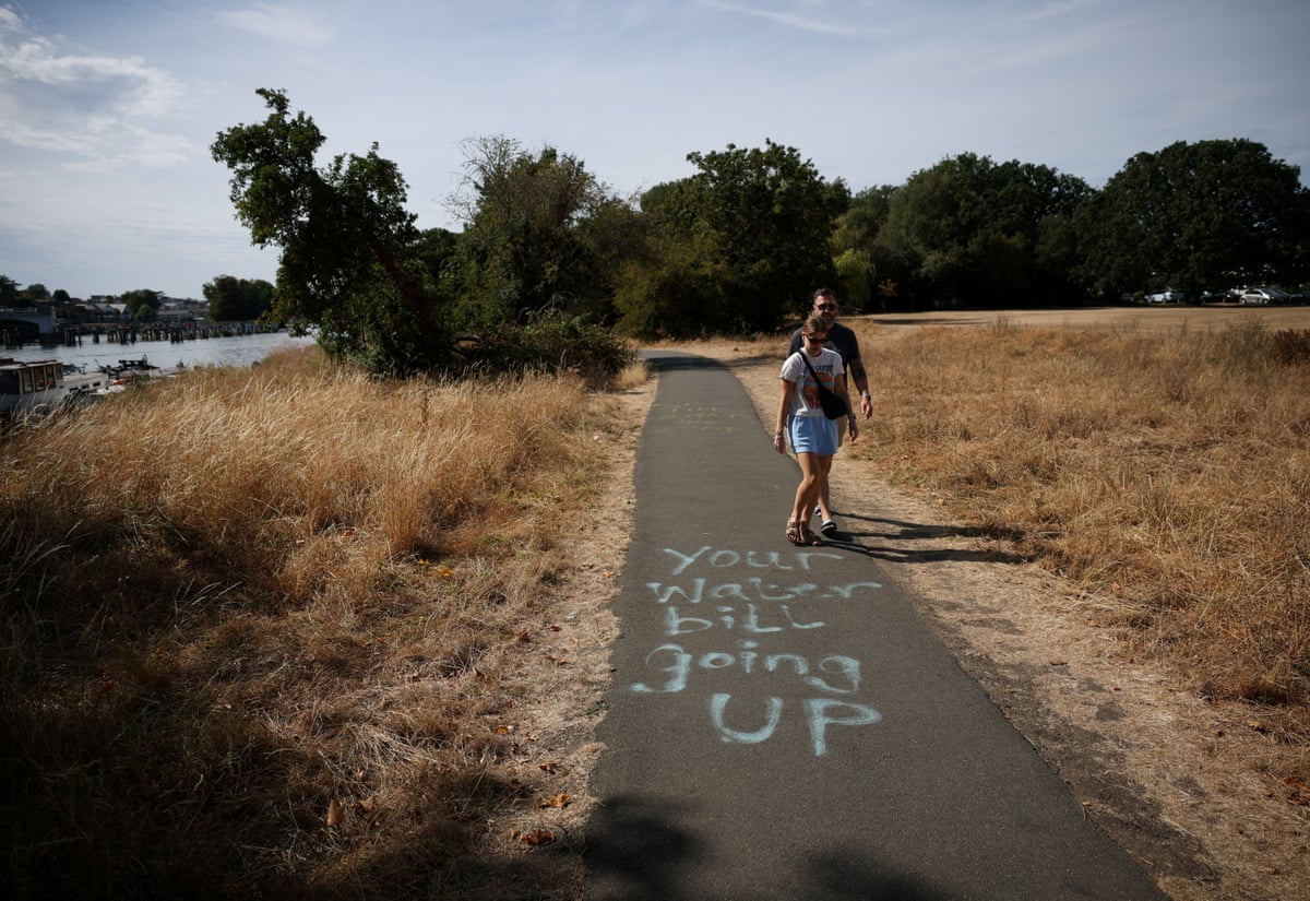 A couple walks past a spray-painted message from the "Save Our Lands and River" community campaign opposing Thames Water's Teddington Direct River Abstraction (TDRA) scheme, which would take 75m litres of drinking water a day from the River Thames at Teddington during droughts and replace it with treated wastewater pumped from Mogden Sewage Treatment Works into the river, in London.