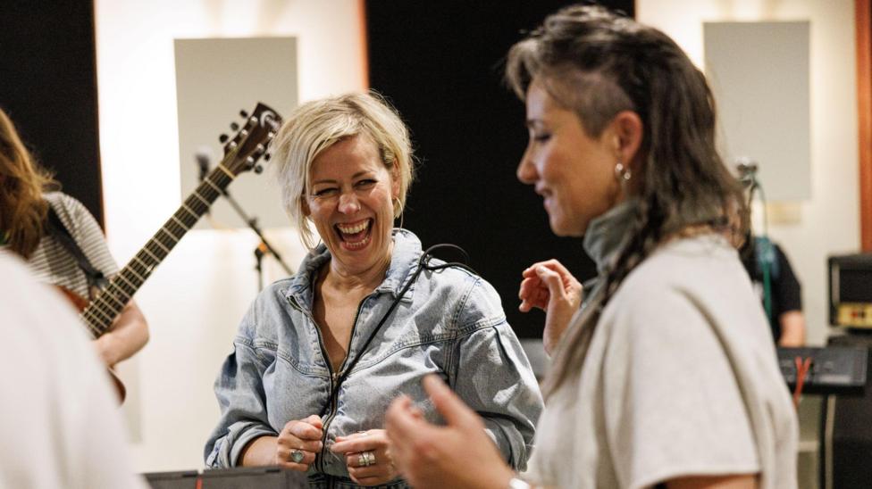Cora Bissett has grey, long-ish hair and is wearing a vintage denim jacket. She is laughing