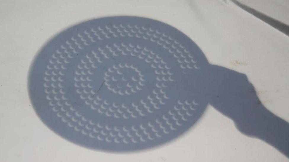 The reflection of a colander on the ground. The holes are in the shape of crescents due to the solar eclipse.