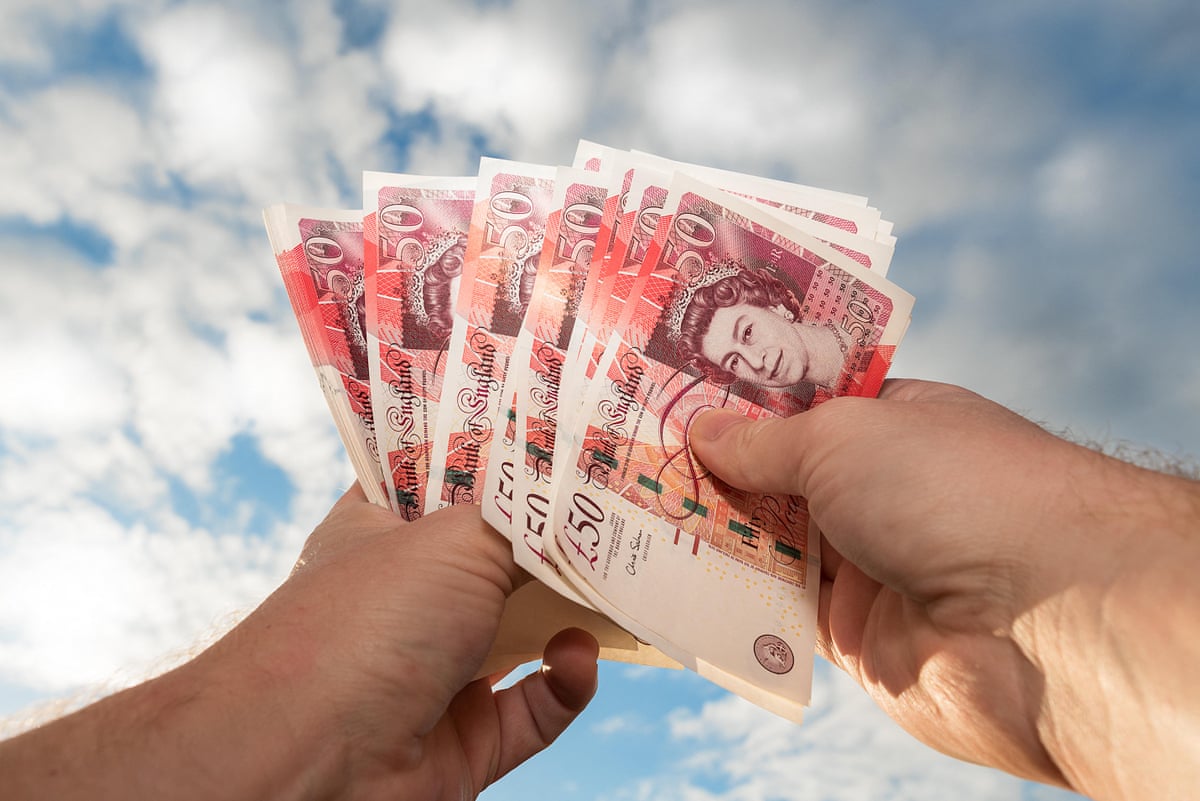Pair of hands counting new style GBP £50 notes sterling with blue sky and cloud background.