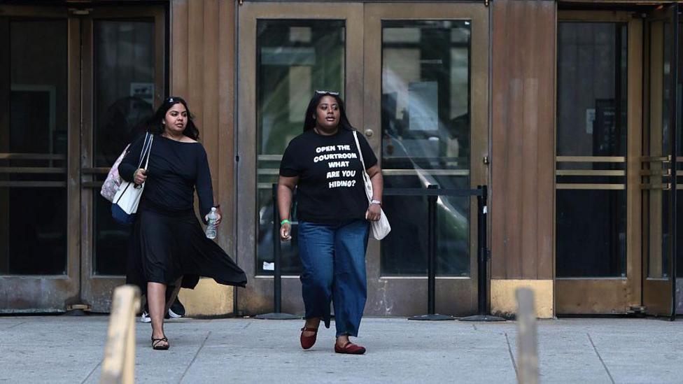 Public spectators leave Mangione's hearing. A woman wears a shirt that says,