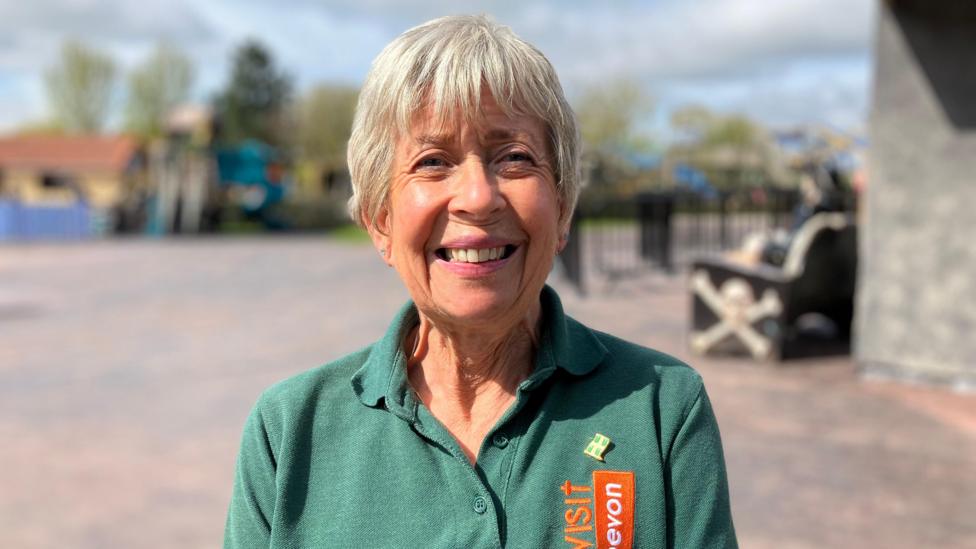 Sally Everton is pictured smiling. She is wearing a green polo shirt with the Visit Devon logo on it.
