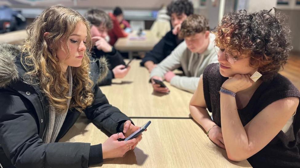 Nina and Evi sitting at a table while one looks at a phone.
