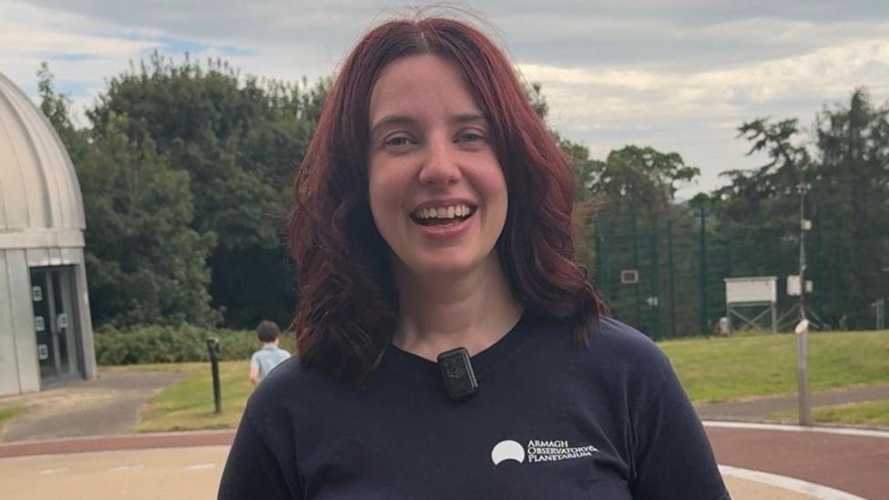 A woman with dark hair smiles at the camera, she is wearing a navy top