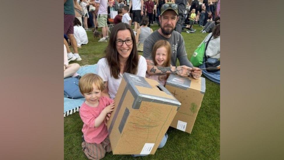 Four people sitting on grass holding cardboard boxes