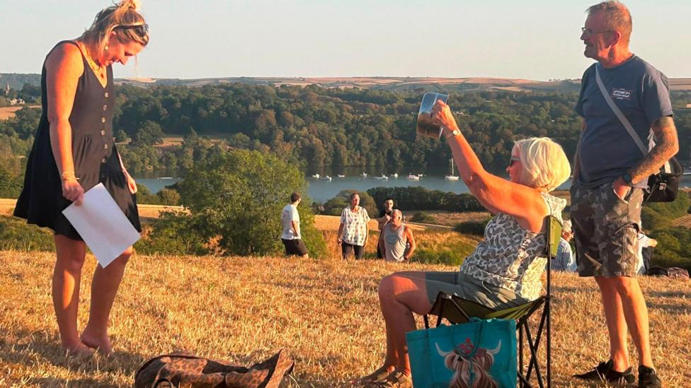 A picture of a number of people gathered in Saltash. There is people sat on a seat.
