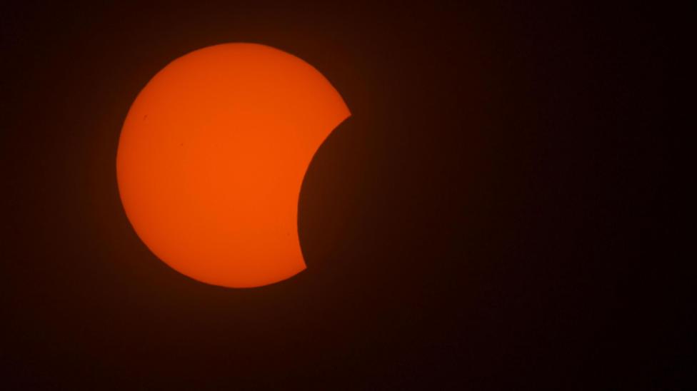 Black silhouette of the Moon passes in front on a red sun