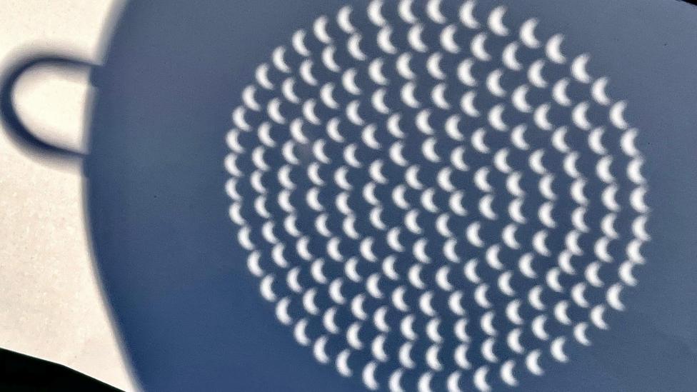 Dozens of partial eclipses as viewed in a reflection, possibly of the projection of the reflection of the Sun and Moon through a colander