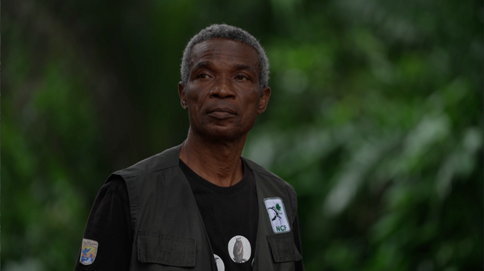 Chukwuemeka Igwe, stands in the sacred forest in Awka-Etiti. He wears an NCF badge on his gilet and a T-Shirt with photos of vultures.