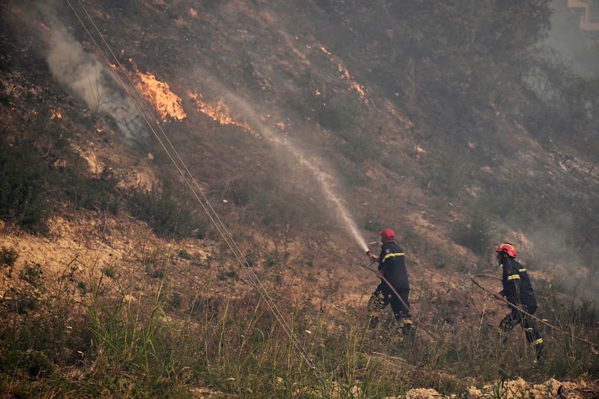 Two firefighters blast water on the side of a hill ablaze with fire.