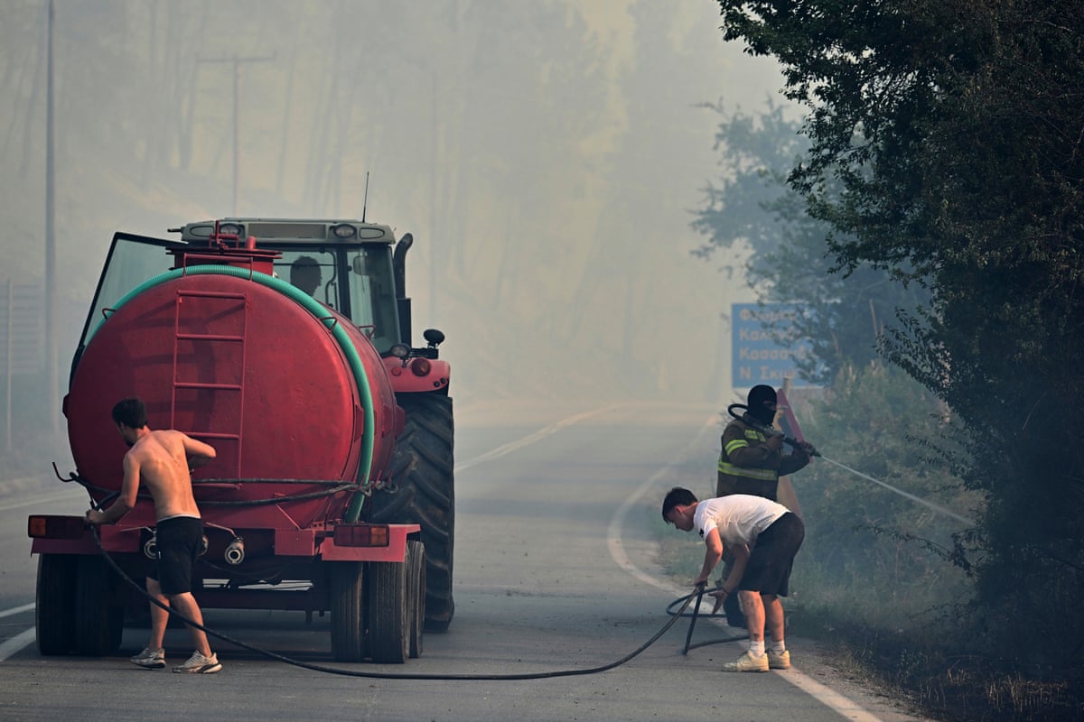 Three people run a hose from a red tank being pulled by a tractor. Smoke hangs in the air.