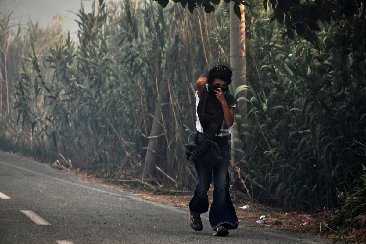 A woman walks along a road covering her face to protect herself from smoke.