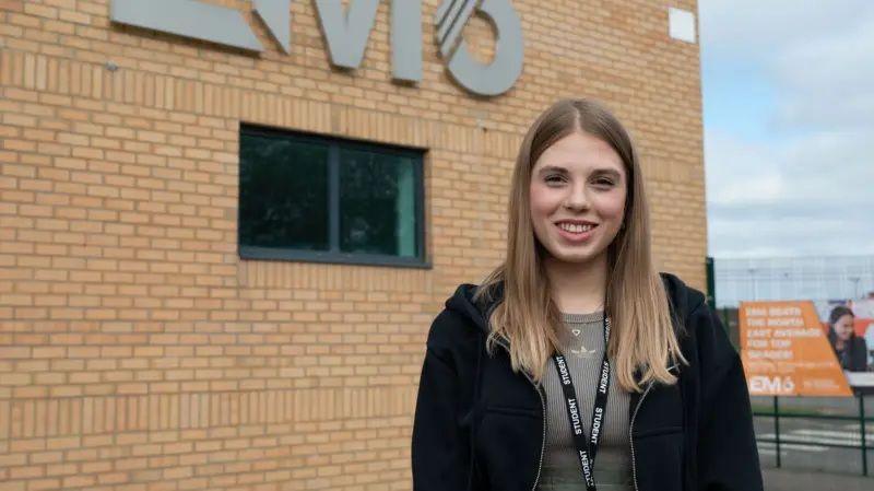 Anastasiia Sochka smiles as she stands outside English Martyrs Catholic School on A-Level results day. She is wearing a black hoodie.