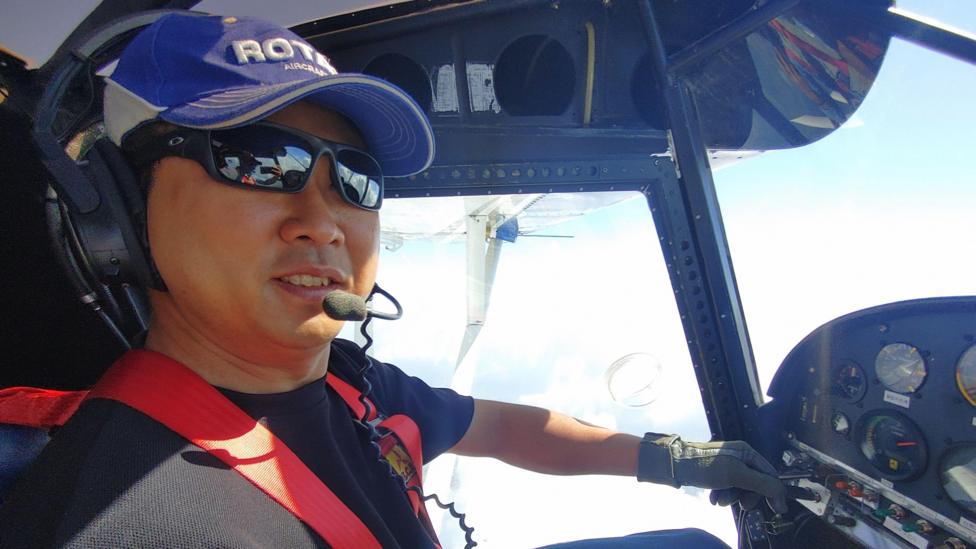 Woongsa Kim, dressed in shades, smiles for the camera while flying a small aircraft