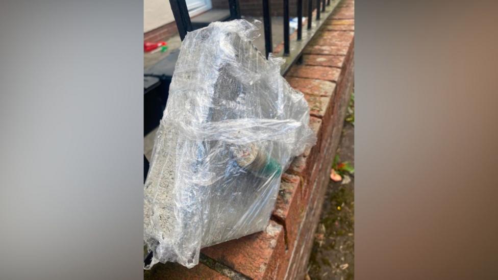 What appears to be a bullet casing and a brick wrapped up in clingfilm on a wall
