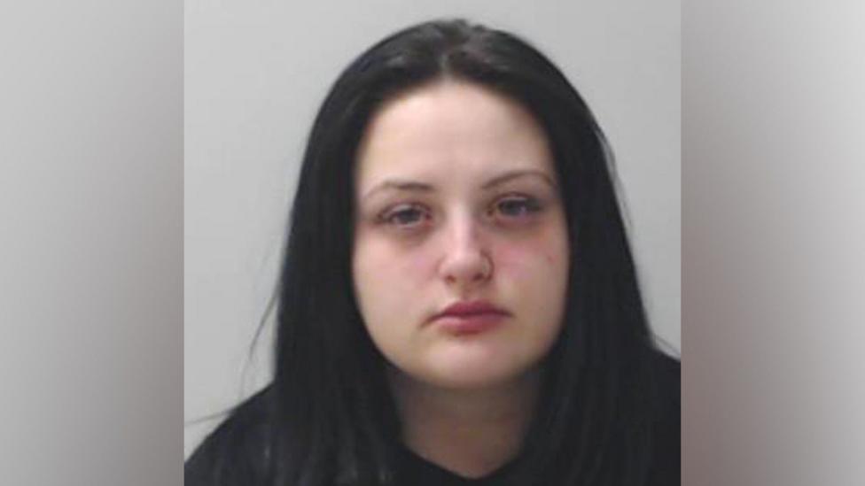 A mugshot of a young woman with long dark hair, looking at the camera.