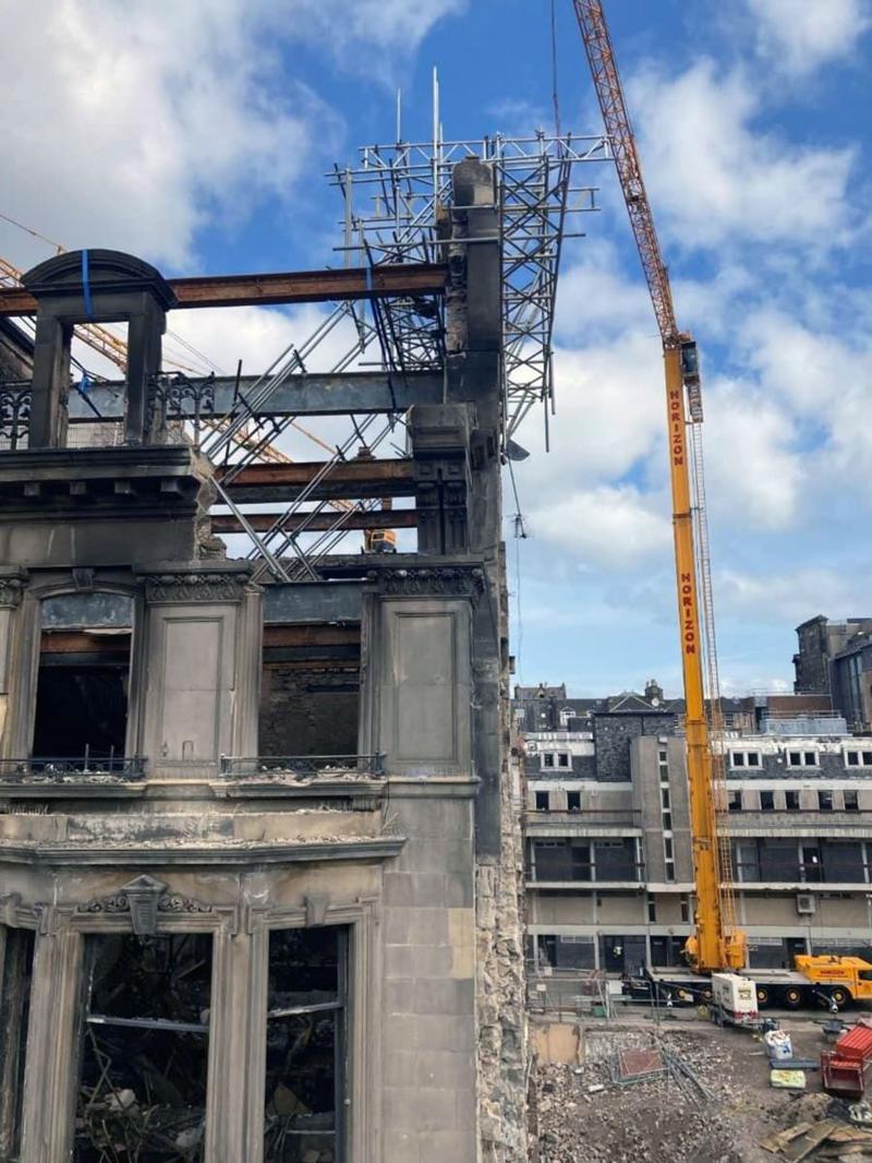 A fire damaged old building with parts of the wall supported by scaffolding and a large yellow crane at one side