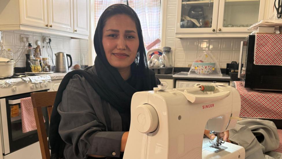 Khadija is sitting at her kitchen table with her sewing machine.