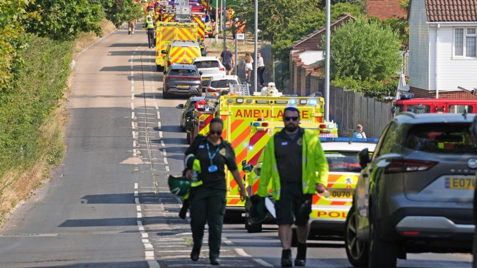 A long line of ambulances and police cars parked on a road parallel to the railway line
