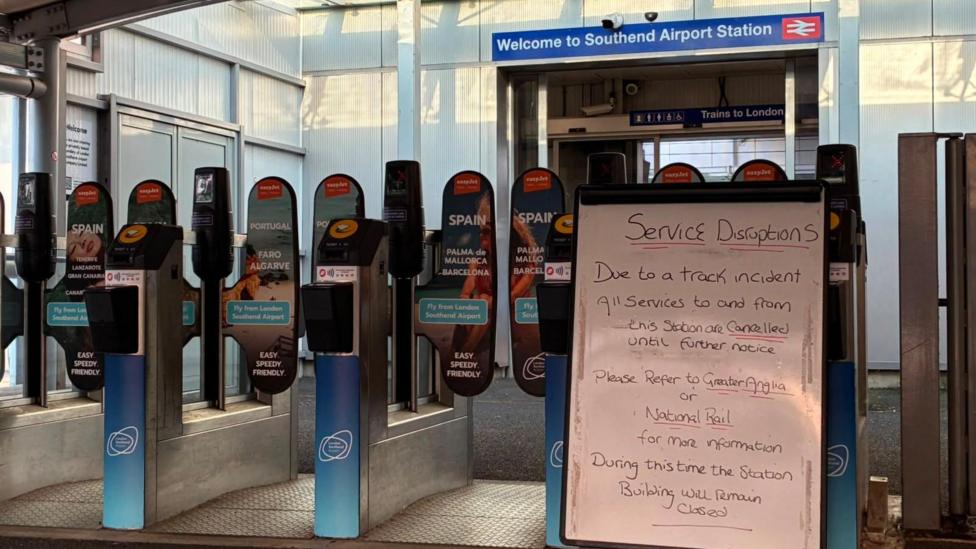 A whiteboard in front of closed railway gates. It says there has been an incident and all services are cancelled until further notice.