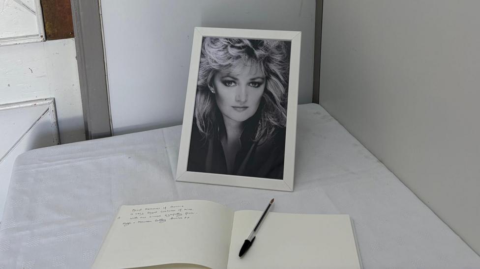 Llun o Bonnie Tyler mewn canolfan tu ôl i lyfr atgofion.