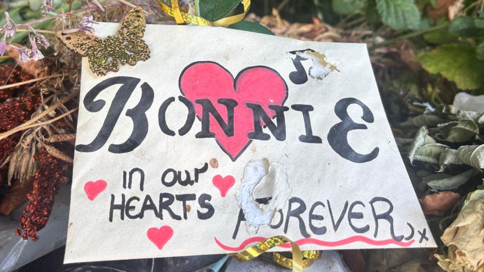 A card with a love heart says 'Bonnie in our hearts forever'