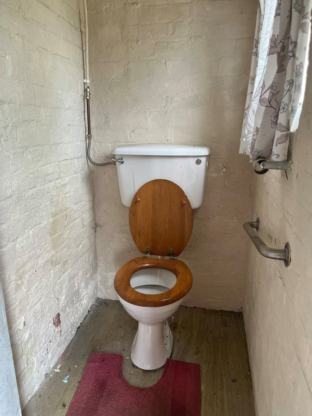 A toilet with crumbling painted brickwork and a bar on the wall