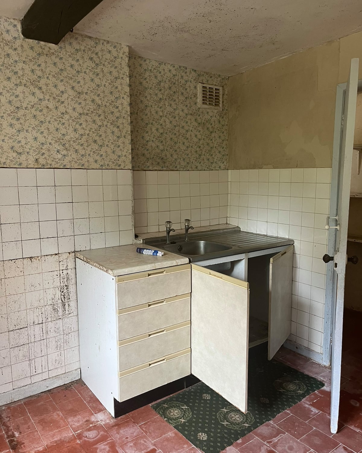 Decrepit-looking kitchen sink area, with tiled floor and black mould on ceiling