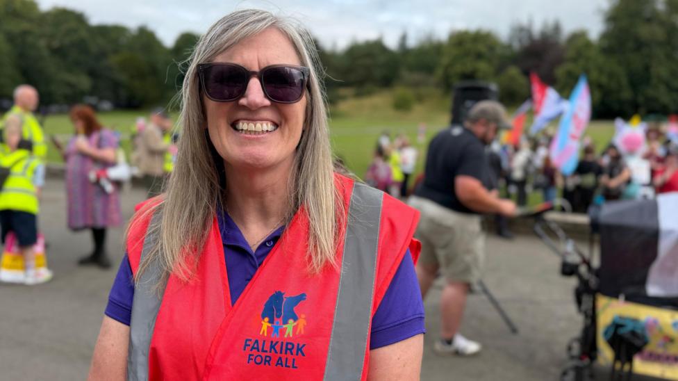 Karen Morrison looking straight at the camera while wearing a red high vis vest. She is smiling and wearing sunglasses