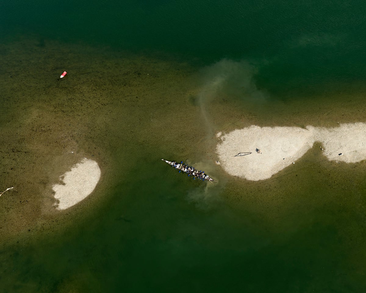 Aerial view of a long rowing boat filled with people in shallow water