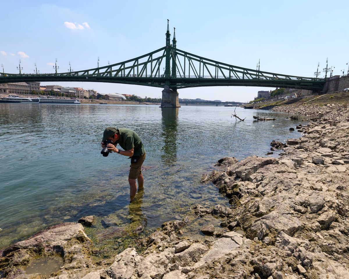A man with his feet in the water bends over to take a picture of the rock