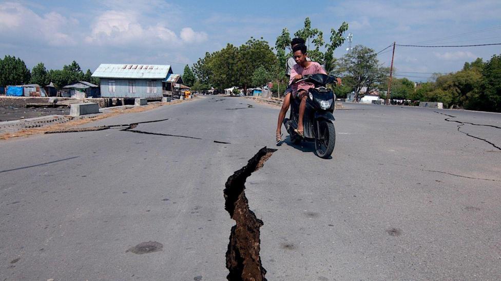 A motorcyclist rides past a crack on the road following the earthquake in East Nusa Tenggara Province, Indonesia.