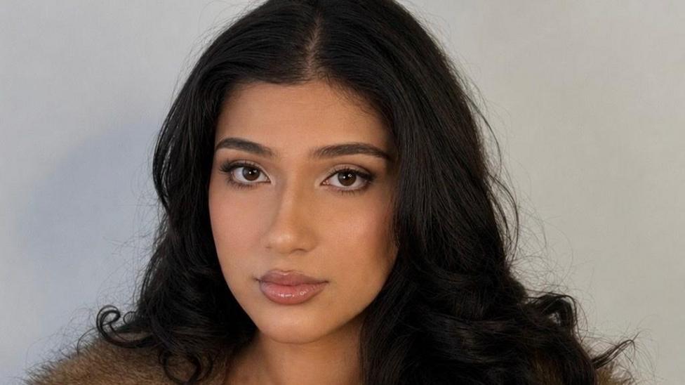 Close up of Wasim who has long hair and brown eyes. She is stood in front of a grey background.