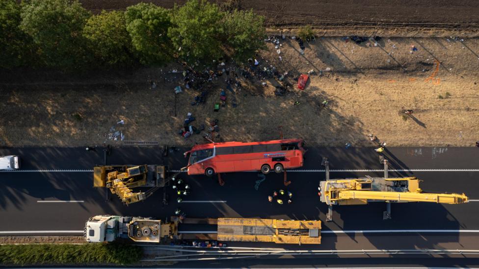 Aerial shot of the bus on the motorway on its side, with cranes beside it.