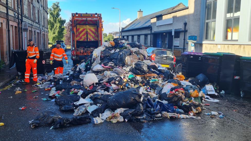 A residential street partially blocked by dumped rubbish.