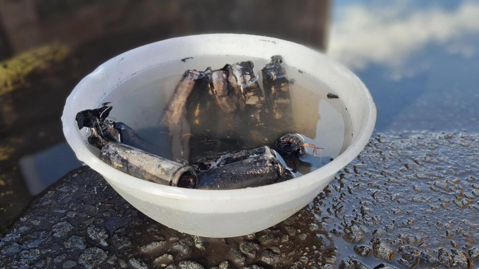 Burnt out batteries in a plastic bowl of water on a road with puddles around it