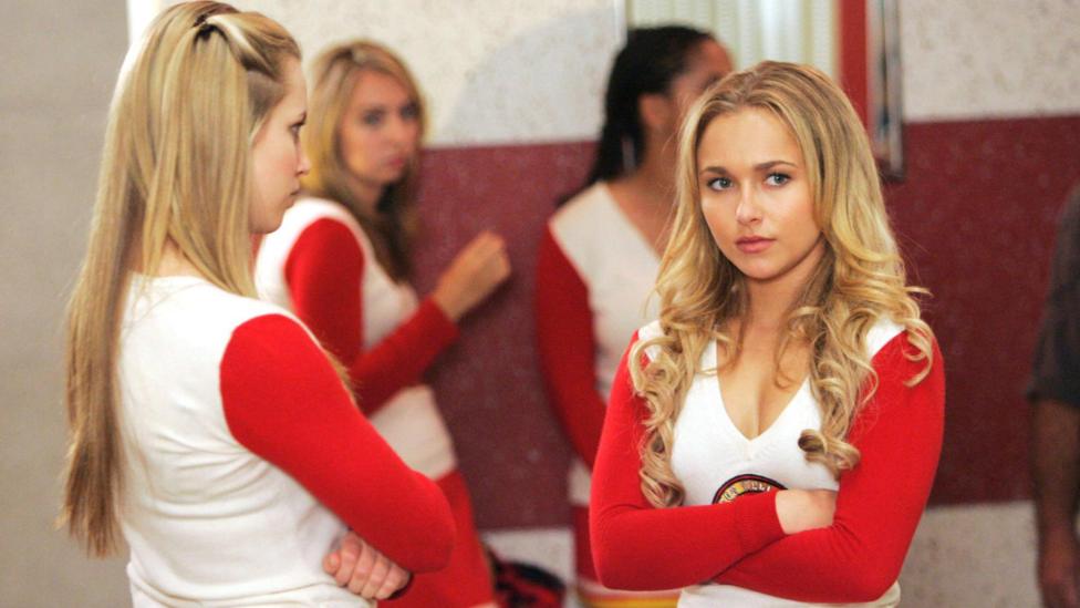 Hayden Panettiere with arms folded in cheerleader's outfit with several other cheerleaders in a scene from Heroes