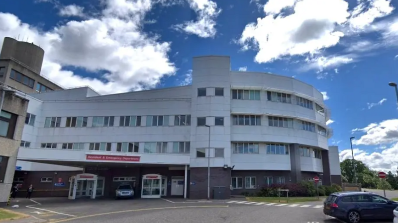A hospital exterior, a large white building with the words Accident and Emergency on a sign