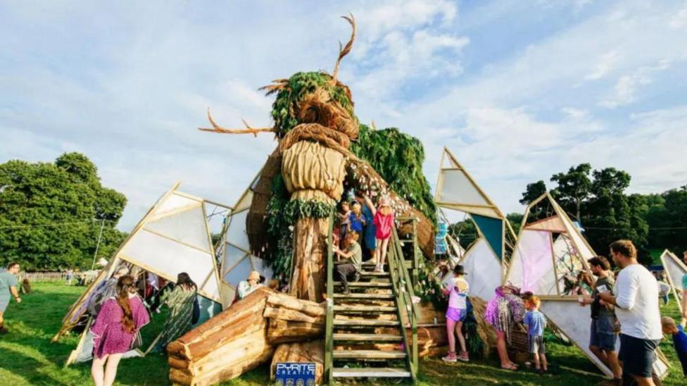Families and children explore a large sculpture of a Green Man.