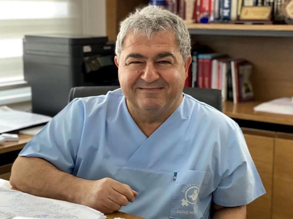 Dr Sevket Alpturk is wearing blue medical scrubs and is sitting a desk, he has short grey hair.