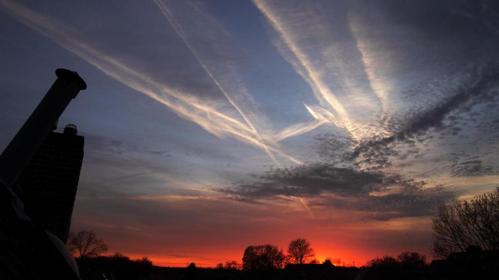 A sky at dusk, with white contrails across the dark blue sky and a red sunset on the horizon